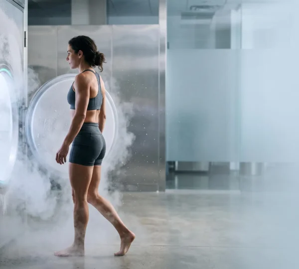Silhouette entrant dans une chambre de cryothérapie corps entier baignée de brume glacée, symbole de récupération et de réduction de l'inflammation