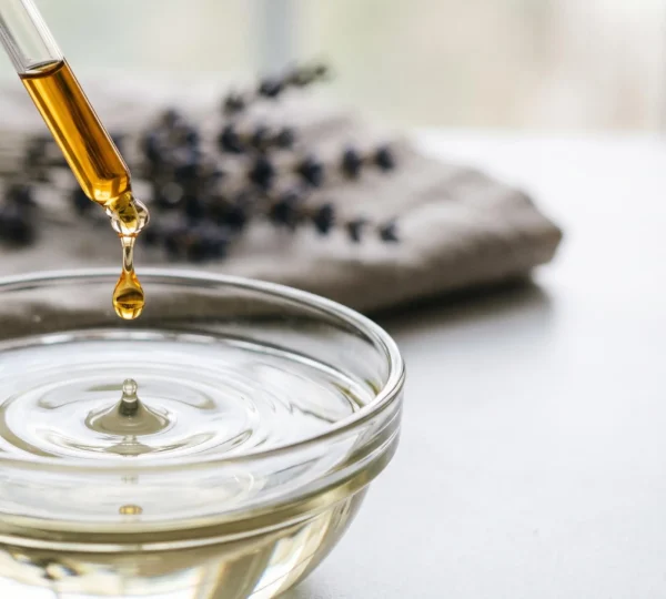 Flacon d'huile essentielle laissant tomber une goutte dans un flacon d'huile végétale, symbole de dilution sécurisée